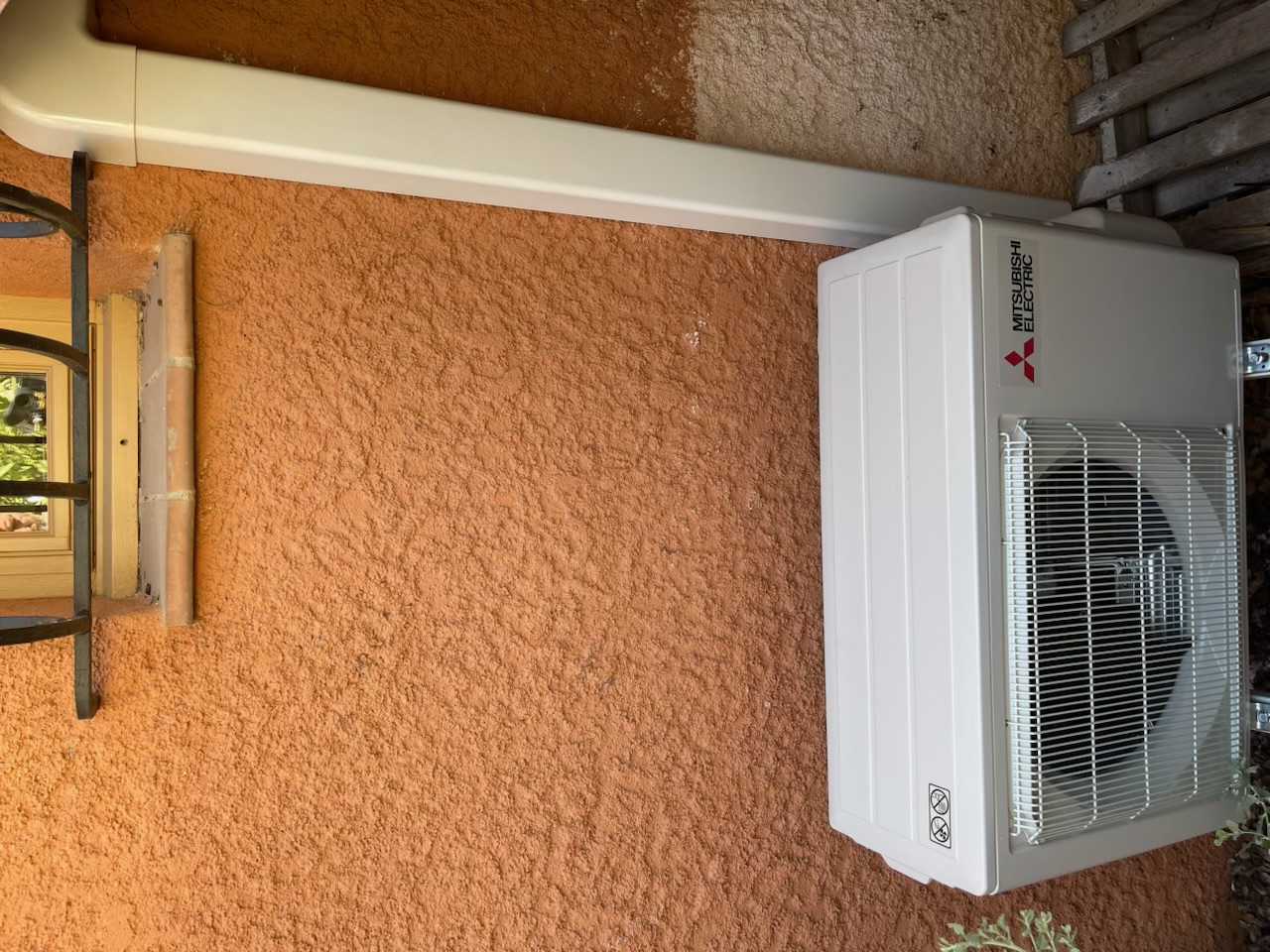 Groupe extérieur Mitsubishi Electric installé sur cale, sous une fenêtre